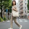 ビジネスカジュアル姿で通勤する20代日本人女性。機能的でおしゃれなトートバッグを持ち、都会の街並みを歩くシーン。